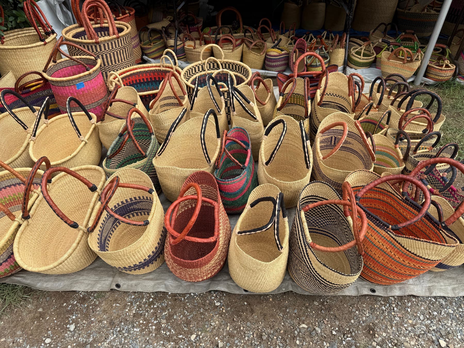 Woven straw sun hats and baskets in purple, tan, and yellow displayed at a Brimfield booth