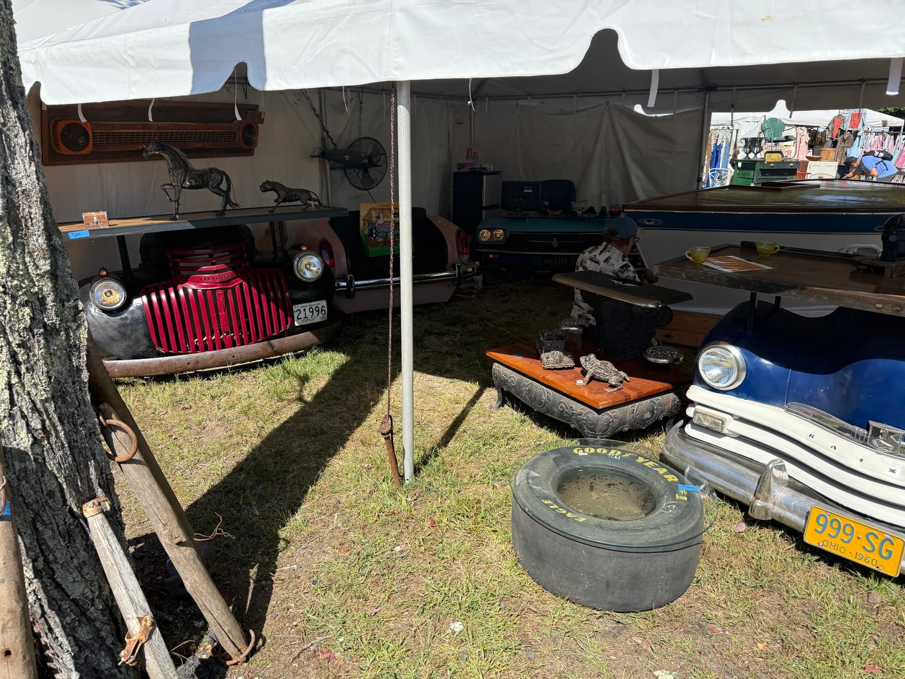 Antique cars repurposed into furniture, with horse and leopard statues, at a Brimfield booth