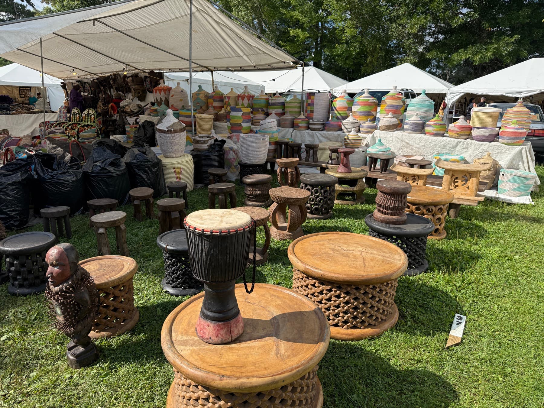 A wide array of African stools, drums, and woven baskets displayed at a Brimfield booth