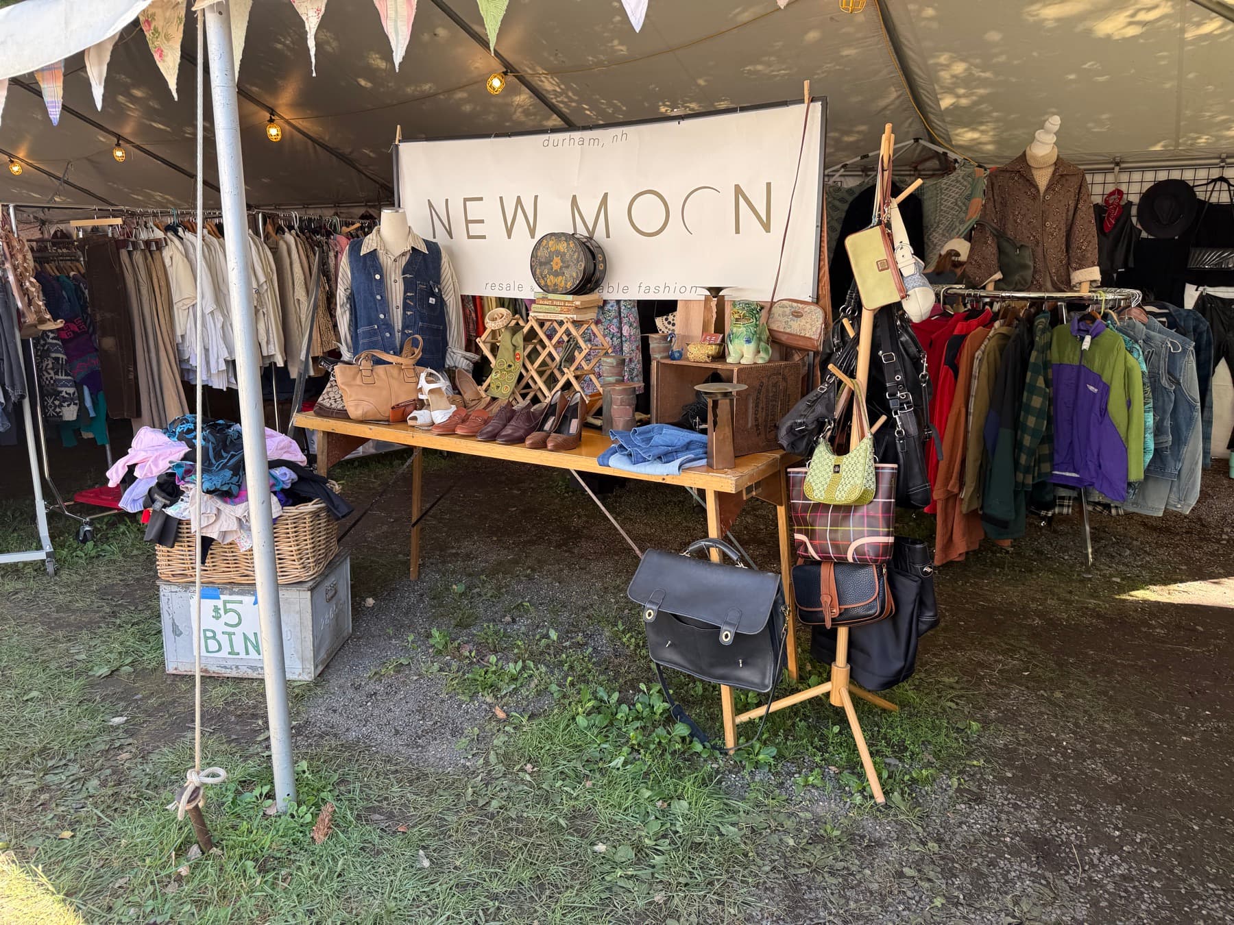 The New Moon resale and sustainable fashion booth banner at Brimfield, with bags and clothing displayed