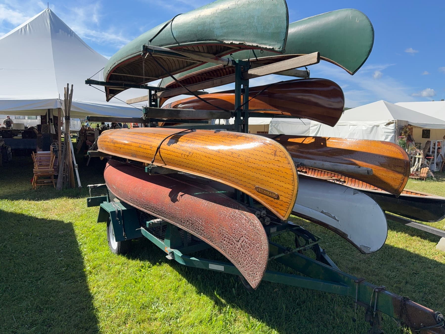 Wooden and fiberglass canoes stacked on a trailer for sale at Brimfield