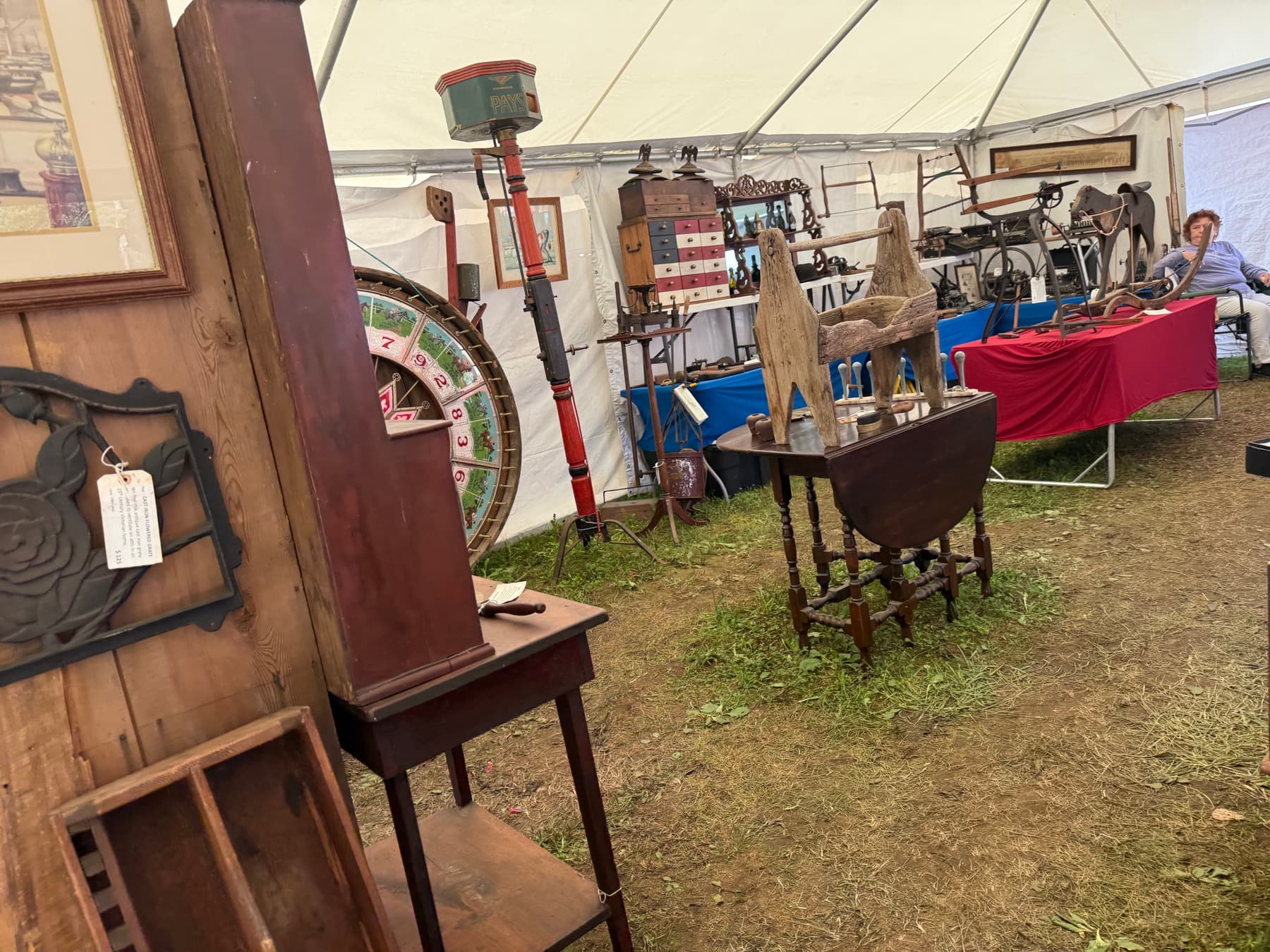 A booth of antique tools, a carnival wheel of fortune, and a horse weathervane at Brimfield