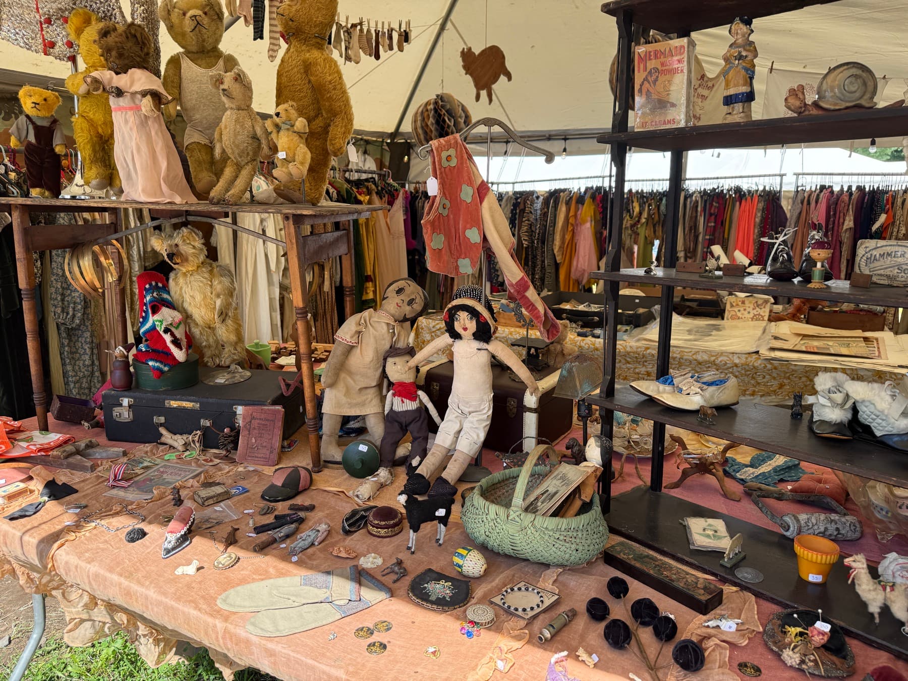 A shelf display of antique teddy bears, dolls, and a Mermaid Washing Powder box at a Brimfield booth