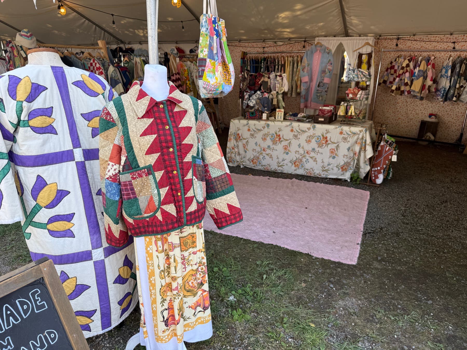 A colorful quilted patchwork jacket and dress displayed on mannequins at a Brimfield booth