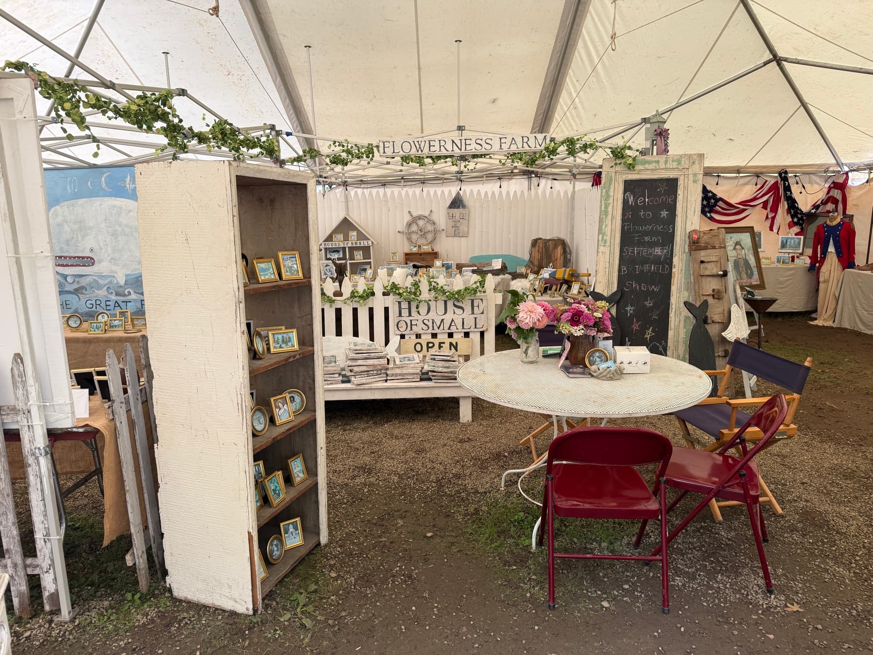 A styled booth with a chalkboard sign welcoming visitors to Flowerness Farm at the Brimfield show