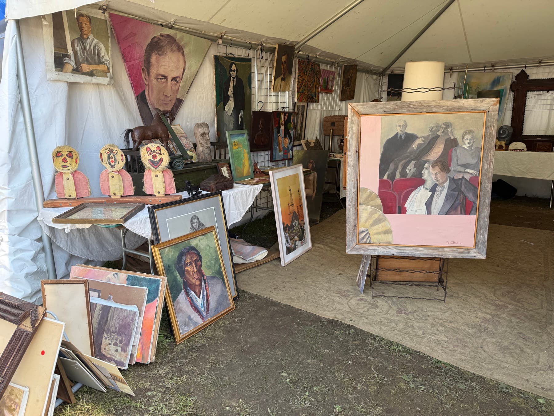 Stacks of vintage paintings and portraits leaning against a table at Brimfield