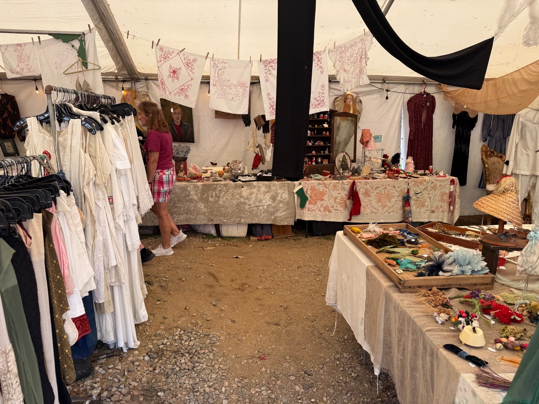 A booth of embroidered vintage linens and clothing racks at Brimfield
